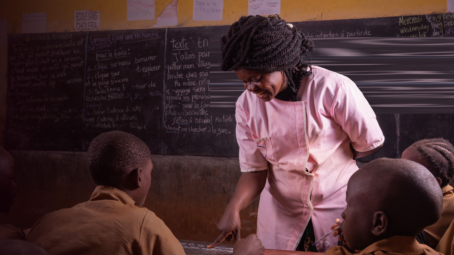 NGO_Black teacher intent on explaining writing on the black board to very attentive pupils By medialensking_envato