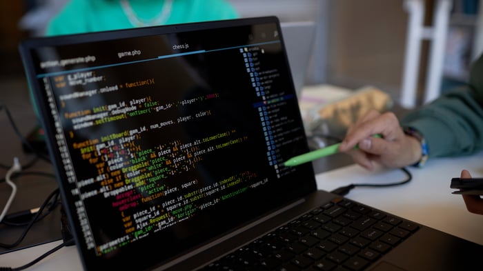 Focus on laptop screen with coded data and pen held by hand of young man