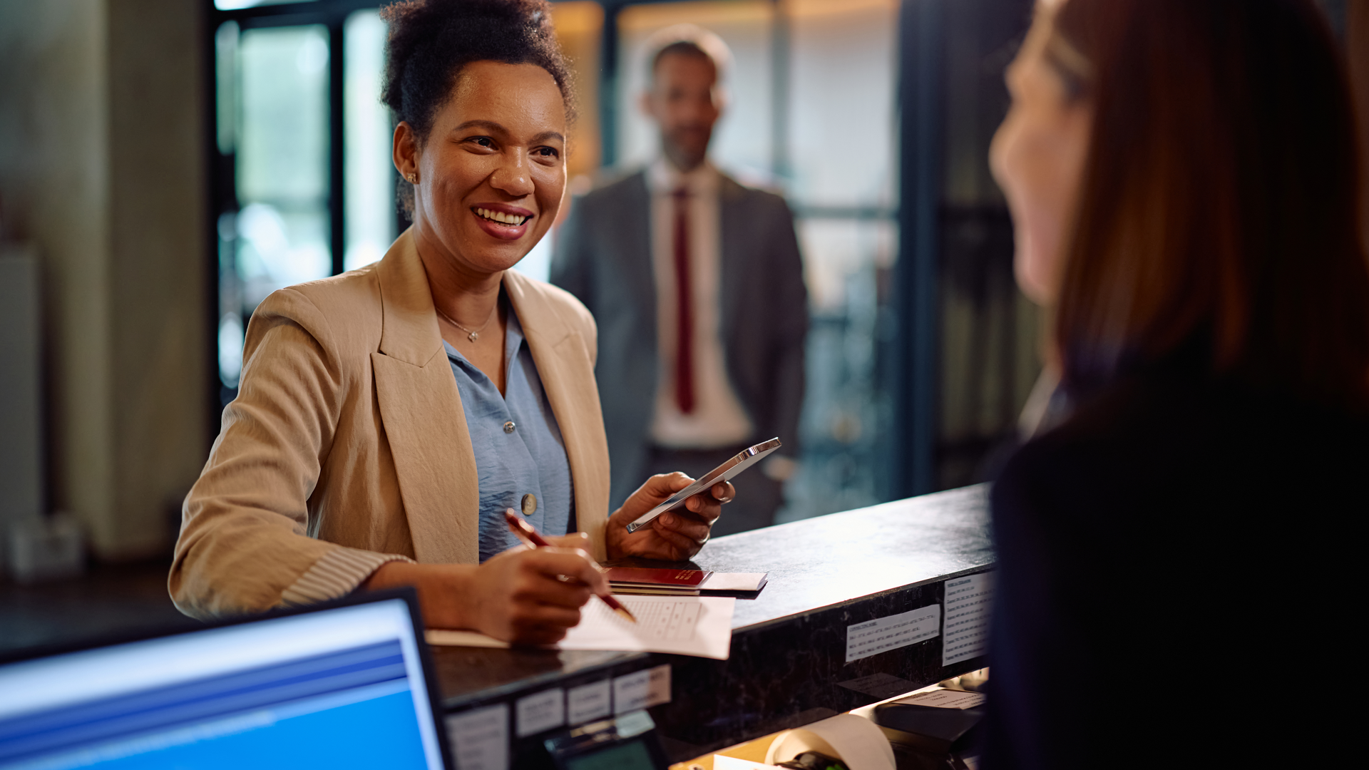 Happy black woman checking in at hotel reception during her business trip. By drazenphoto_L1