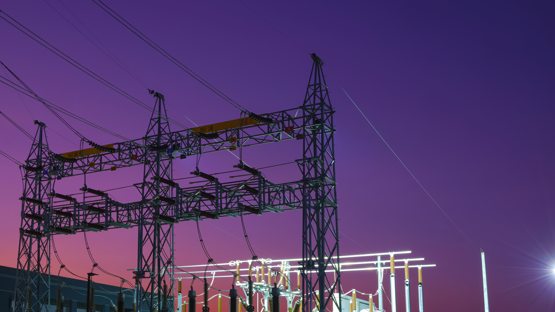 Silhouette of high voltage electric pylons with electrical equipment of power substation at night